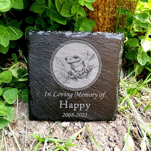 May include: Black slate memorial stone with a frog illustration and the text "In Loving Memory of Happy 2008-2025".