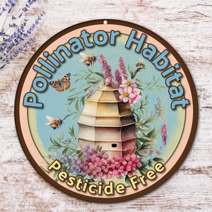 May include: A round, brown wooden sign with a light blue background and the text "Pollinator Habitat Pesticide Free". The sign features a beehive surrounded by flowers and bees.