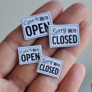 May include: Four small white signs with black text. Two signs say "Come in We're Open" and two signs say "Sorry We're Closed".