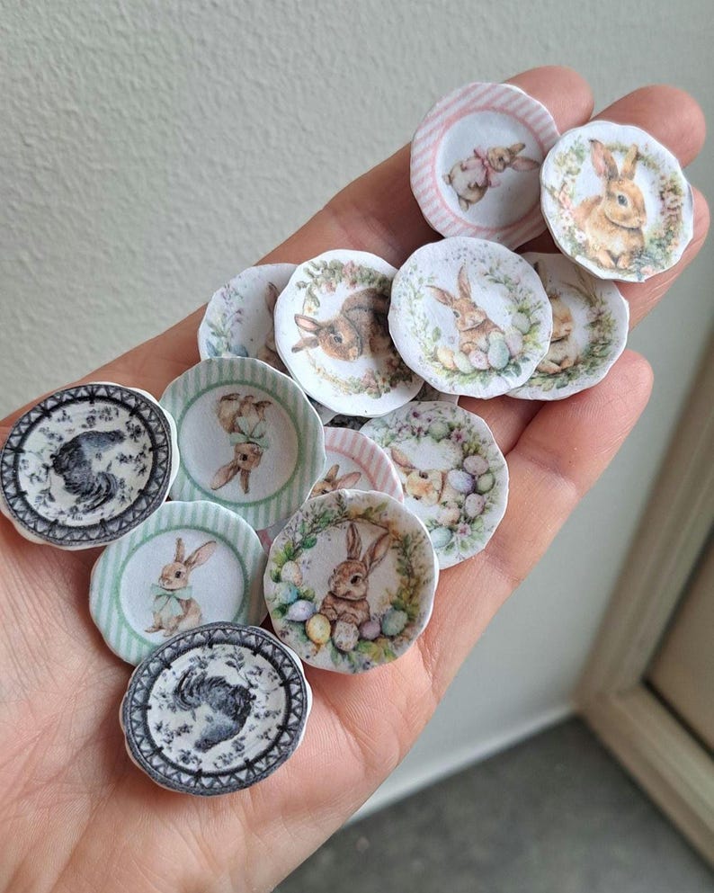 May include: A collection of miniature decorative plates featuring Easter bunny designs. The plates have various pastel color schemes, including pink, green, and white, with floral and striped borders. The bunny illustrations vary in style and detail.
