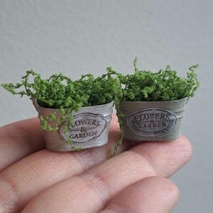 Op de afbeelding: Twee miniatuur metalen bloempotten met groen mos en de tekst "Flowers & Garden" aan de voorkant.