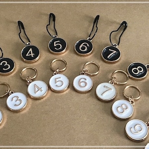 Könnte beinhalten: Ein Satz mit 10 schwarzen und weißen nummerierten Reißverschluss-Zierbändern mit goldenen Ringen. Die Zahlen 2 bis 9 sind sowohl in Schwarz als auch in Weiß dargestellt.