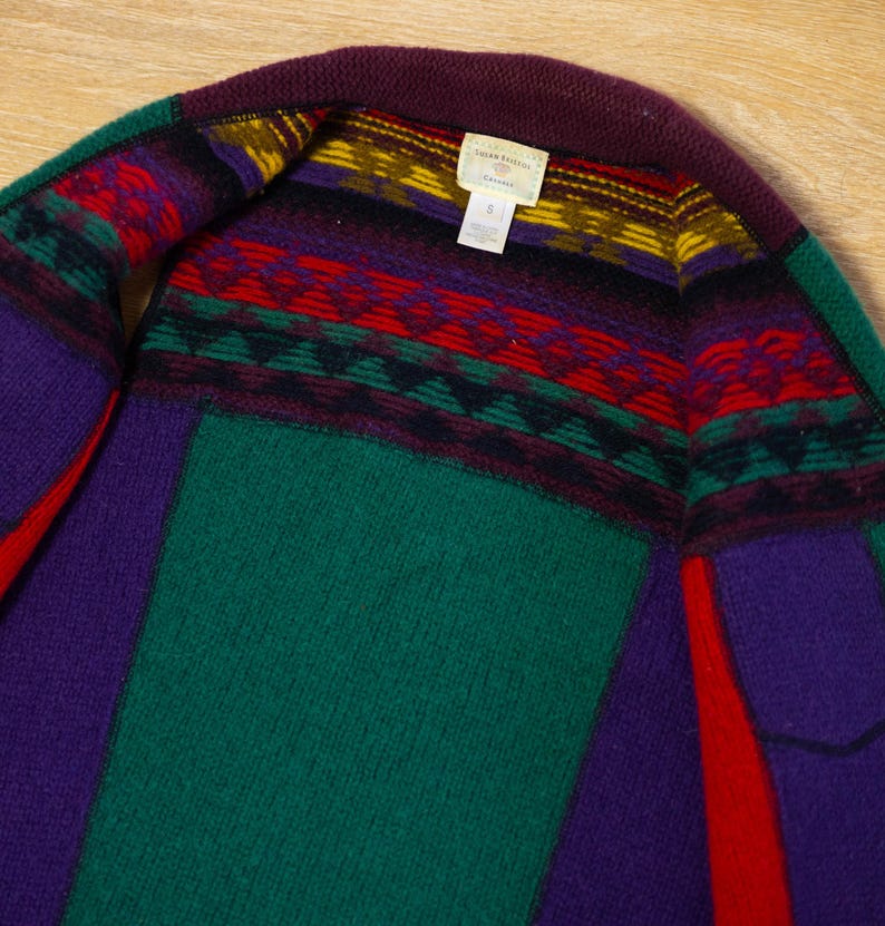 May include: A green, purple, and red striped cardigan with a geometric pattern around the neckline. The label reads "Lauren Ralph Lauren,  Cardigan".