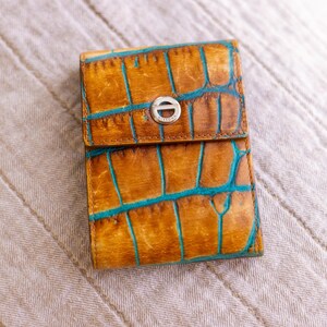 May include: A brown leather wallet with a blue crocodile pattern and a silver metal clasp. The wallet has a fold-over flap and a small pocket on the front.