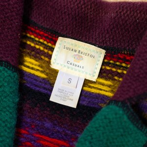 May include: A close-up of a brown, green, purple, yellow, and red striped fleece jacket with a tag that reads "Susan Bristol Casuals" and "S".