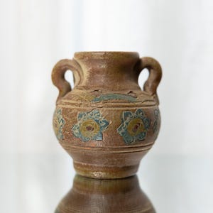 Könnte beinhalten: Eine braune Keramikvase mit zwei Henkeln und einem Blumendesign. Die Vase hat eine hellbraune Glasur mit blauen und gelben Akzenten.