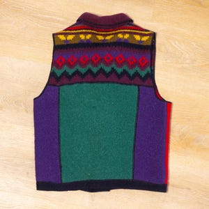 May include: A sleeveless knitted vest with a colorful geometric pattern. The vest is made of a thick, warm wool blend and features a burgundy, purple, green, and yellow color scheme.