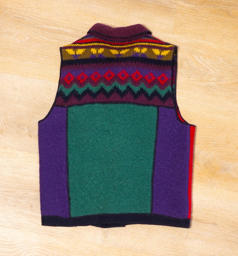 May include: A sleeveless knitted vest with a colorful geometric pattern. The vest is made of a thick, warm wool blend and features a burgundy, purple, green, and yellow color scheme.