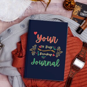 May include: A blue journal with the text "Your 30 Day Breakup Journal" in colourful lettering with a heart and floral design.