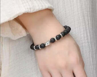 May include: Black lava rock beaded bracelet with a silver Buddha charm.