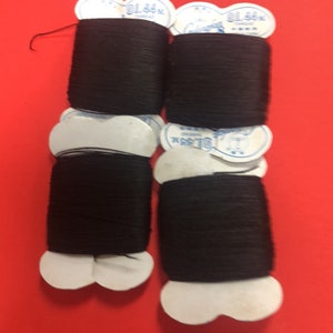May include: Four spools of black thread on a red background. Each spool is labeled with a white tag. The thread is tightly wound, and the tags have text and a small design.