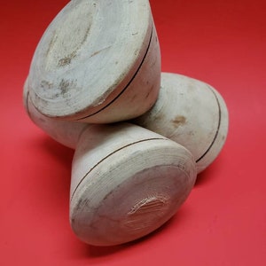 Könnte beinhalten: Drei Holz-Kreisel, jeder mit einer dunkelbraunen Linie um die Mitte, sind übereinander gestapelt. Die Kreisel sind hellbraun und haben eine glatte, leicht abgenutzte Oberfläche.