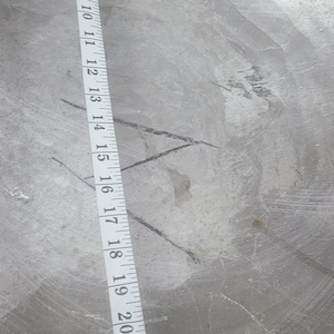 Könnte beinhalten: Ein weißes Maßband mit schwarzen Markierungen, das Zoll von 2 bis 24 anzeigt. Das Band ist an einer grauen, strukturierten Oberfläche angebracht.