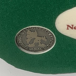 Puede incluir: Una moneda de metal de color plateado con las palabras "The Best of Mickey Collection" alrededor del borde. En el centro de la moneda hay una silueta de Mickey Mouse.