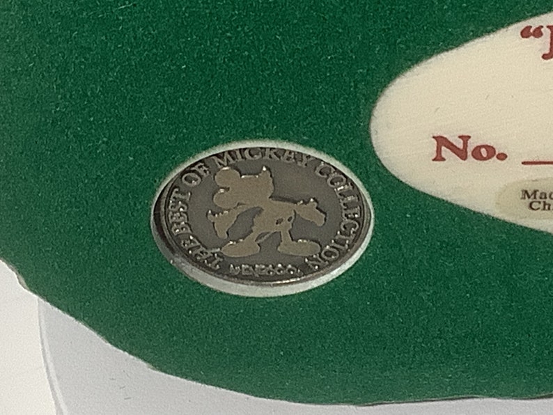 Puede incluir: Una moneda de metal de color plateado con las palabras "The Best of Mickey Collection" alrededor del borde. En el centro de la moneda hay una silueta de Mickey Mouse.