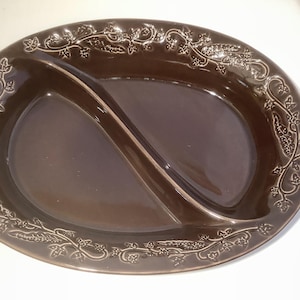 May include: An oval-shaped, dark brown ceramic serving dish featuring a central divider that splits the interior into two distinct sections. The wide rim is decorated with a raised, embossed pattern of trailing ivy leaves and vines.