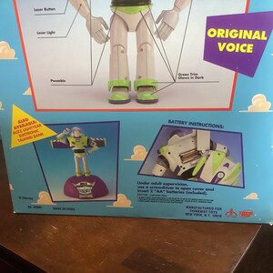 Op de afbeelding: Een speelgoeddoos met Buzz Lightyear uit Toy Story. De doos is lichtblauw met afbeeldingen van het personage en de tekst "Original Voice". Het bevat een kleine afbeelding van het speelgoed en batterij-instructies.