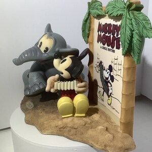 Puede incluir: Un conjunto de figuras que representa a Mickey Mouse tocando el acorde&oacute;n, un elefante gris y un cartel que dice "Mickey Mouse in Jungle Rhythm".