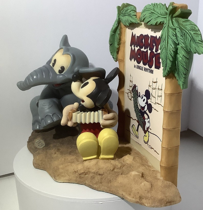Puede incluir: Un conjunto de figuras que representa a Mickey Mouse tocando el acorde&oacute;n, un elefante gris y un cartel que dice "Mickey Mouse in Jungle Rhythm".