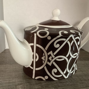May include: A ceramic teapot with a brown body and white accents. The teapot features a white spout, handle, and lid. The brown body is decorated with a white geometric pattern. The teapot is designed for brewing and serving tea.
