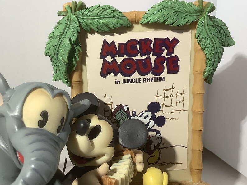 Puede incluir: Un conjunto de figuras que presenta a Mickey Mouse y un elefante gris. Mickey est&aacute; tocando un acorde&oacute;n y lleva una camisa roja y negra. El elefante est&aacute; de pie junto a Mickey. El conjunto est&aacute; delante de un cartel que dice "Mickey Mouse in Jungle Rhythm".