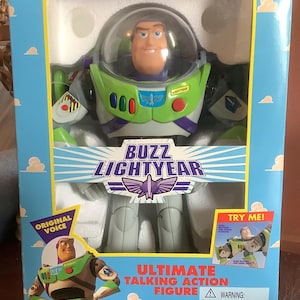 Op de afbeelding: Buzz Lightyear Ultimate Talking Action Figuur in een doos. De figuur zit in een doos met een blauwe lucht en wolken. De figuur draagt een groen en wit ruimtepak met een doorzichtige helm. Op de doos staan de woorden "Buzz Lightyear" en "Original Voice".