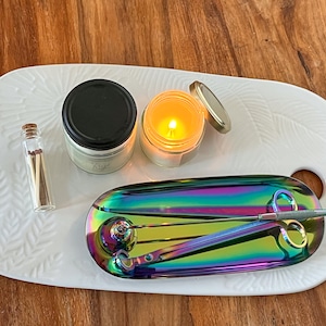 May include: A white ceramic tray with a candle, a jar of matches, and a small iridescent tray with a candle snuffer and a pair of tweezers.