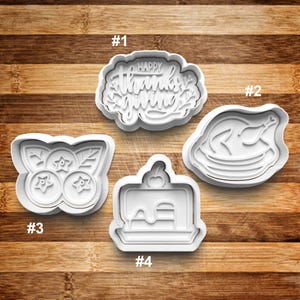 May include: Four white plastic cookie cutters, numbered 1 through 4.  #1 is a Happy Thanksgiving cookie cutter. #2 is a turkey cookie cutter. #3 is a blueberry cookie cutter. #4 is a cake cookie cutter.