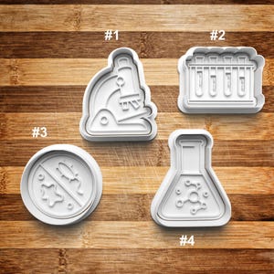 May include: Four white plastic cookie cutters shaped like a microscope, test tubes, a no germs sign, and a beaker with molecules. The cutters are numbered 1 through 4.