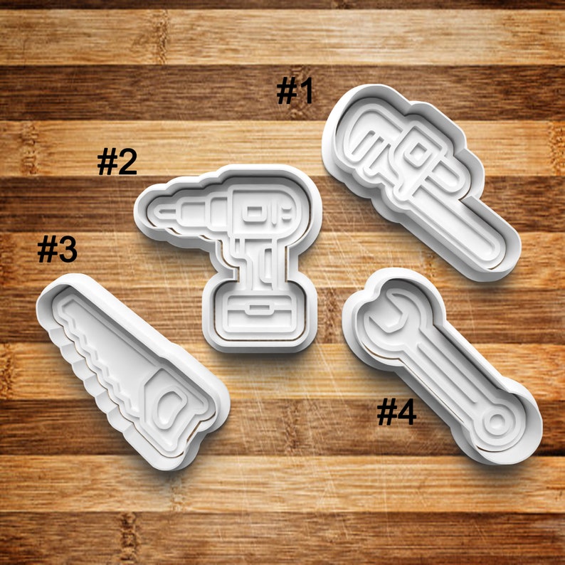 May include: Four white plastic cookie cutters shaped like tools: a wrench, a saw, a drill, and a pipe wrench. The cutters are numbered 1 through 4.