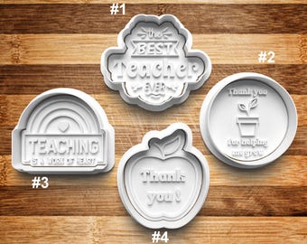 May include: Four white plastic cookie cutters with teacher-themed designs. The cutters feature the phrases "The Best Teacher Ever", "Thank You for Helping Me Grow", "Teaching is a Work of Heart", and "Thank You".