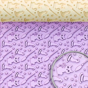 May include: A light-colored wooden rolling pin with an engraved pattern of cats, witch hats, broomsticks, and stars. The rolling pin is positioned above a light purple surface displaying the same repeating pattern, with a circular magnifying glass.