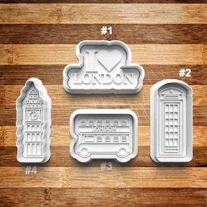 May include: Four white plastic cookie cutters shaped like London landmarks: a double-decker bus, a phone booth, Big Ben, and a sign that says "I Love London" with a heart.