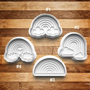 May include: Four white plastic rainbow cookie cutters with different designs. The cutters are numbered 1 through 4.  The cutters are on a wooden surface.