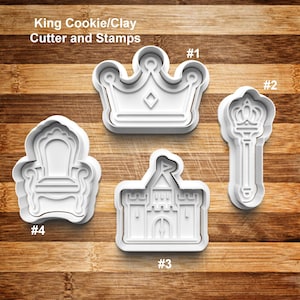 May include: White plastic cookie cutters and stamps in the shape of a crown, scepter, castle, and throne. The text "King Cookie/Clay Cutter and Stamps" is at the top. The cutters are on a wooden surface.