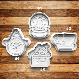 May include: Four white plastic cookie cutters shaped like a snowman, a snow globe, a house, and a teacup. The cutters are numbered 1 through 4.