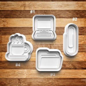 May include: Four white plastic cookie cutters shaped like a laptop, paperclip, folder, and coffee cup. The cutters are numbered 1 through 4.