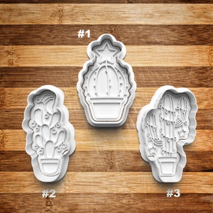May include: Three white plastic cookie cutters shaped like cacti with Christmas decorations. The cutters are numbered 1, 2, and 3.
