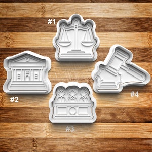 May include: Four white plastic cookie cutters shaped like legal symbols: a scale of justice, a courthouse, a gavel, and a judge's bench with three figures. The cutters are numbered 1 through 4.