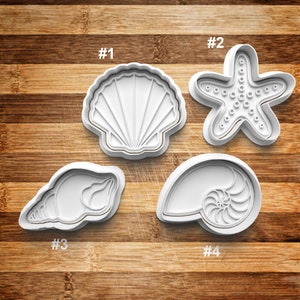 May include: Four white plastic cookie cutters shaped like seashells and a starfish. The cutters are numbered 1 through 4.