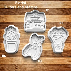 May include: A collection of white plastic cookie cutters and stamps with a florist theme. The set includes a florist shop, a bouquet of flowers, a potted flower, and a pair of pruning shears. The text "Florist Cutters and Stamps" is at the top.