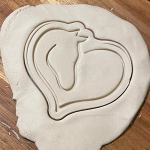 May include: A heart-shaped cookie cutter with a horse silhouette inside. The cutter is made of metal and is ready to be used to cut out cookies.