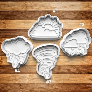 May include: Four white plastic cookie cutters shaped like weather elements: a sun behind a cloud, a cloud with snowflakes, a tornado, and a cloud with raindrops. The cutters are numbered 1 through 4.