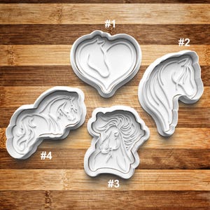 May include: Four white plastic cookie cutters shaped like horses. The cutters are numbered 1 through 4. Cutter #1 is a heart shape with a horse inside. Cutter #2 is a horse's head. Cutter #3 is a horse's head with a mane. Cutter #4 is a horse running.