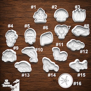May include: A collection of sixteen white plastic cookie cutters featuring various sea life shapes including a coral, seashell, seahorse, jellyfish, lobster, fish, crab, dolphin, seal, whale, shark, and sand dollar, labeled with numbers one through sixteen.