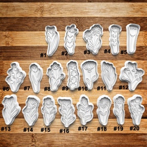 May include: Twenty white plastic cookie cutters shaped like different flowers and leaves. The cutters are numbered 1 through 20.