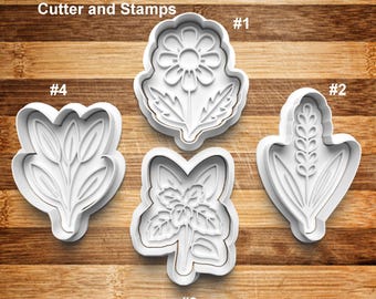 May include: Four white plastic cookie cutters and stamps in various herb and floral designs. The cutters include a daisy, a sprig of wheat, a sprig of leaves, and a floral design. The text "Herbs Cookie/Clay Cutter and Stamps" is at the top.