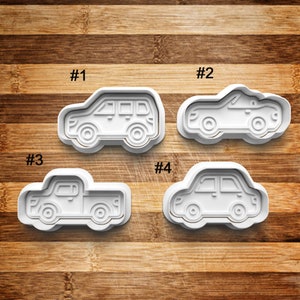 May include: Four white plastic cookie cutters shaped like different types of cars: a van, a sports car, a pickup truck, and a sedan. The cutters are numbered 1 through 4.
