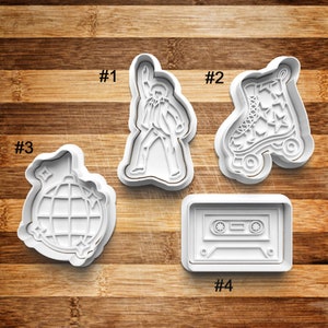 May include: Four white plastic cookie cutters shaped like a disco ball, roller skate, cassette tape, and a person dancing. The cutters are numbered 1 through 4.