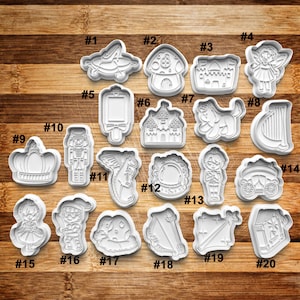 May include: Twenty white plastic cookie cutters in various shapes, including a crown, a nutcracker, a castle, a fairy, a mushroom, a carriage, a dragon, a mirror, a knight, a sword, a wand, and a gingerbread house. The cutters are numbered 1 through 20.